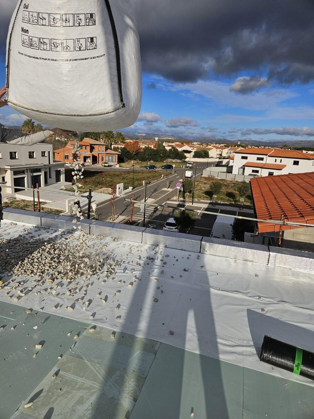 Le gravier levé à la grue au-dessus de la toiture (toitures-terrasses d'une maison neuve)